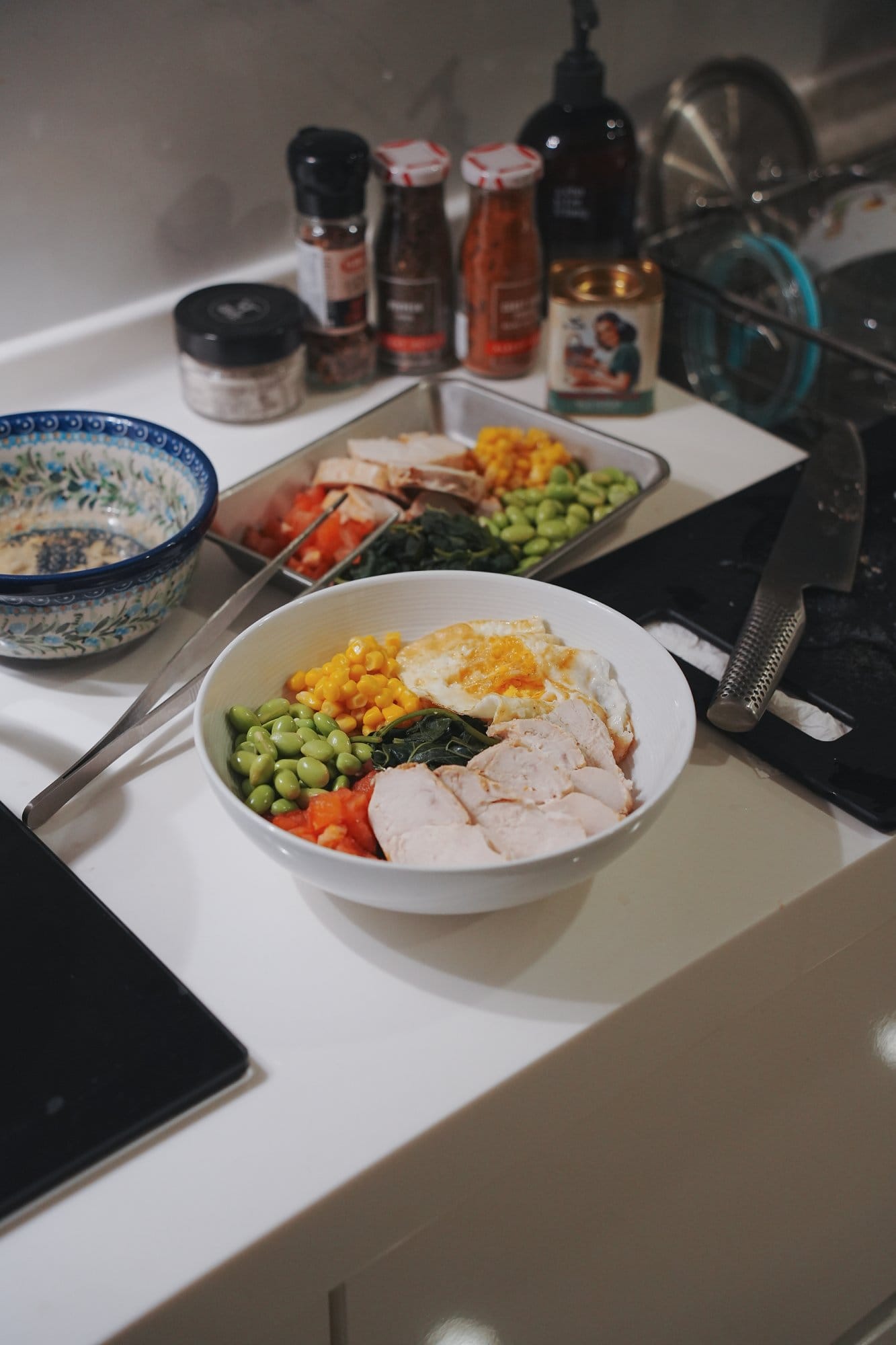 A bowl of chicken rice topped with corn, edamame, spinach and a fried egg on a kitchen counter