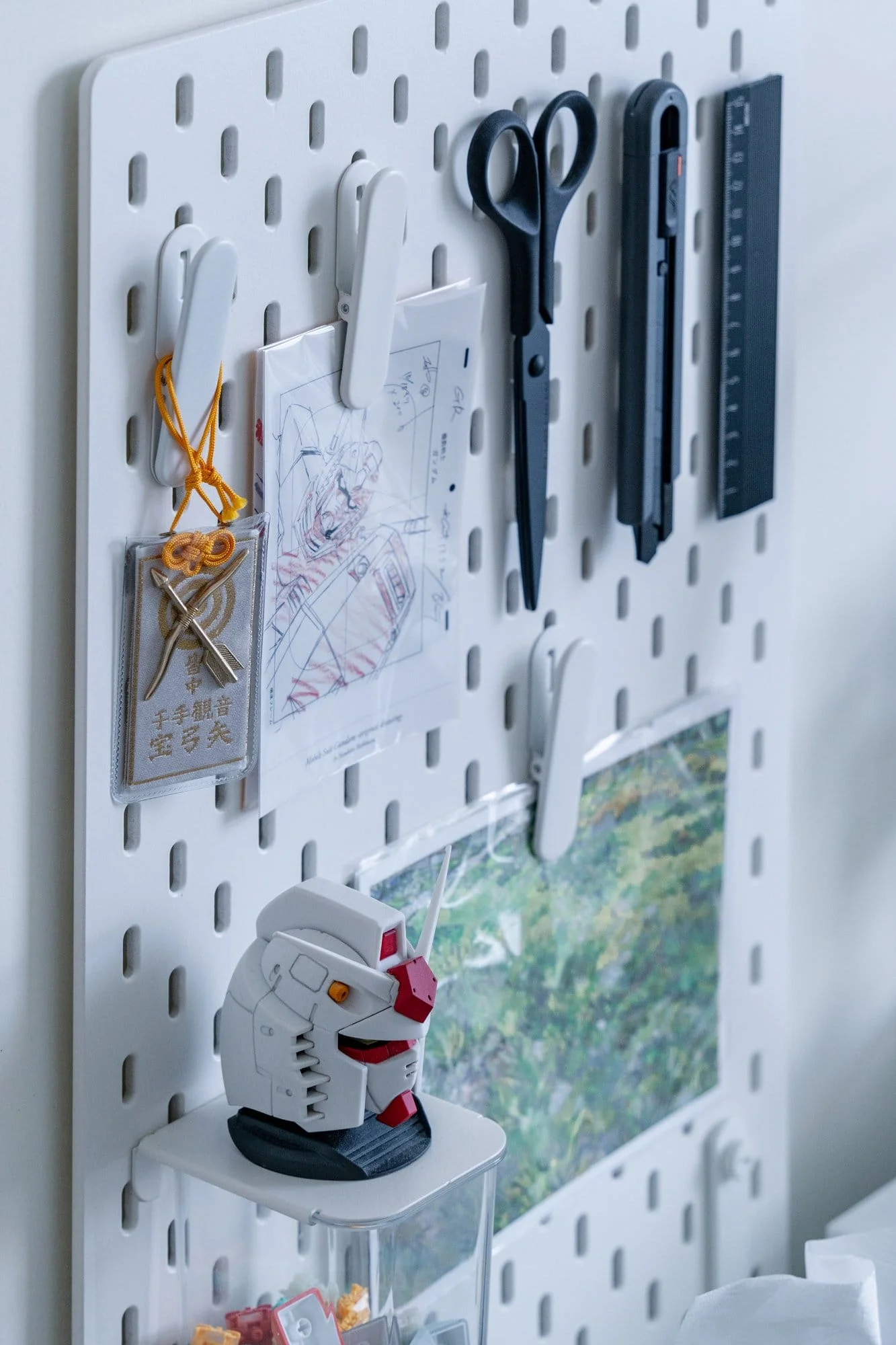 A pegboard holding Gundam sketches, cutting tools and a model head
