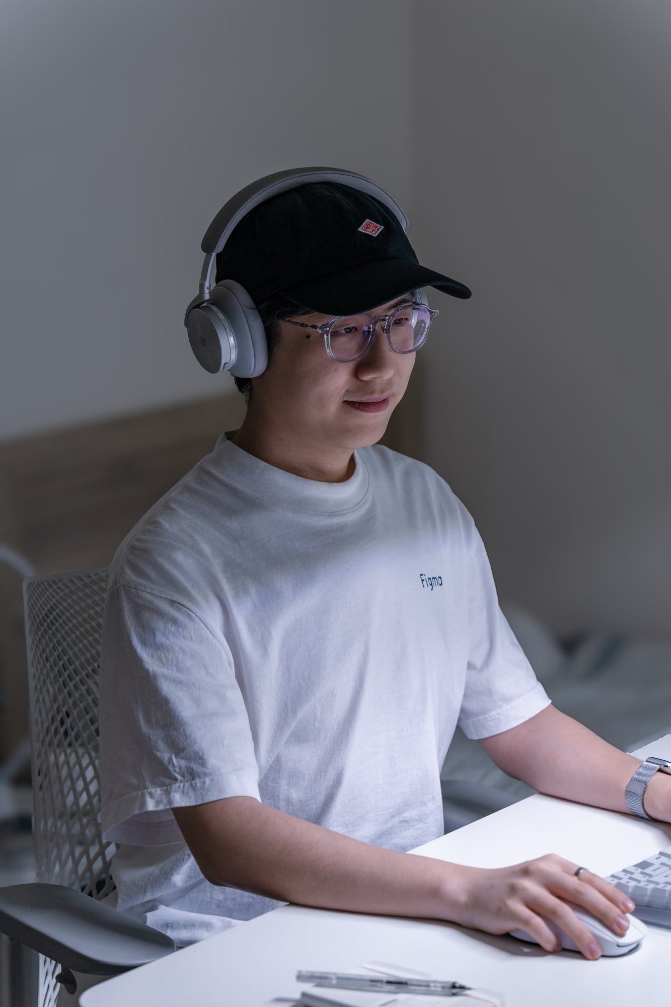 A photo portrait of a man wearing B&O H95 headphones seated on a Herman Miller Sayl chair at his desk