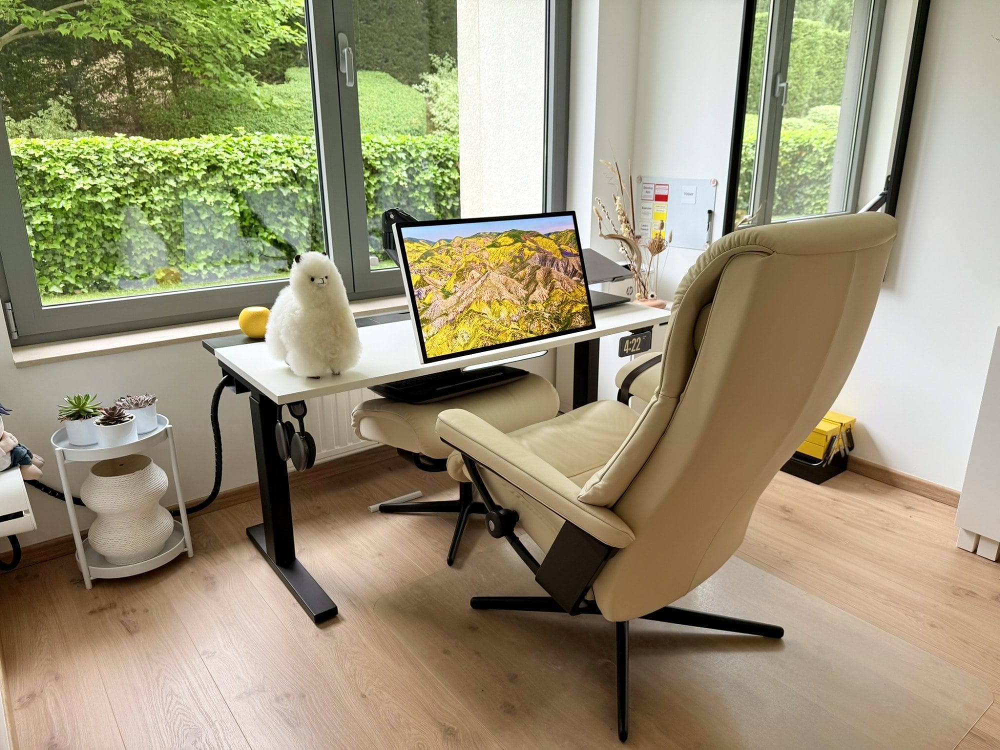 A zero gravity home office desk setup with an Apple Studio Display, Stressless View chair, and toy alpaca by the window