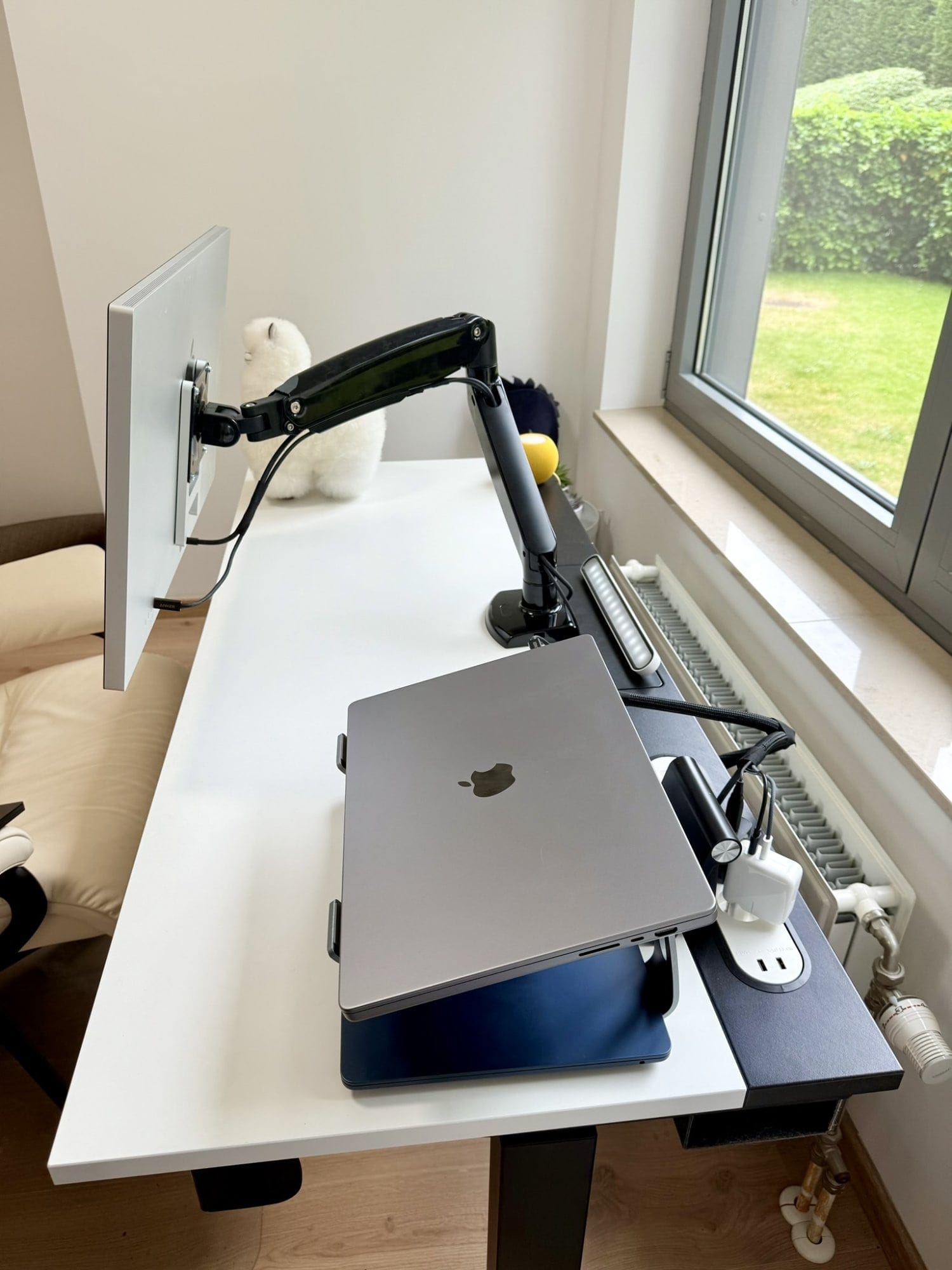 A side desk view with a MacBook on stand and Apple Studio Display on monitor arm