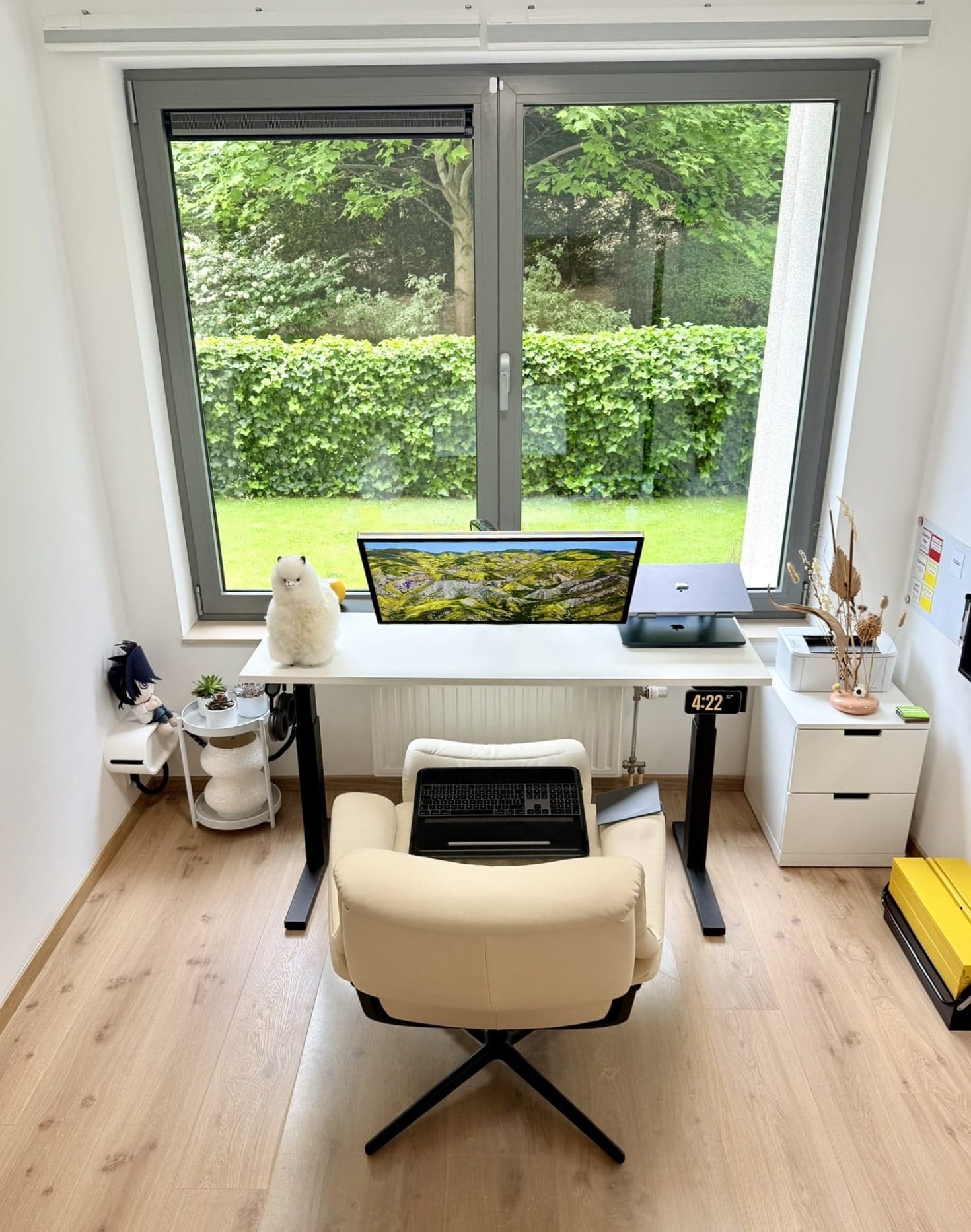 A desk setup with a beige reclining chair, Apple Studio Display, MacBook Pro, and plush alpaca
