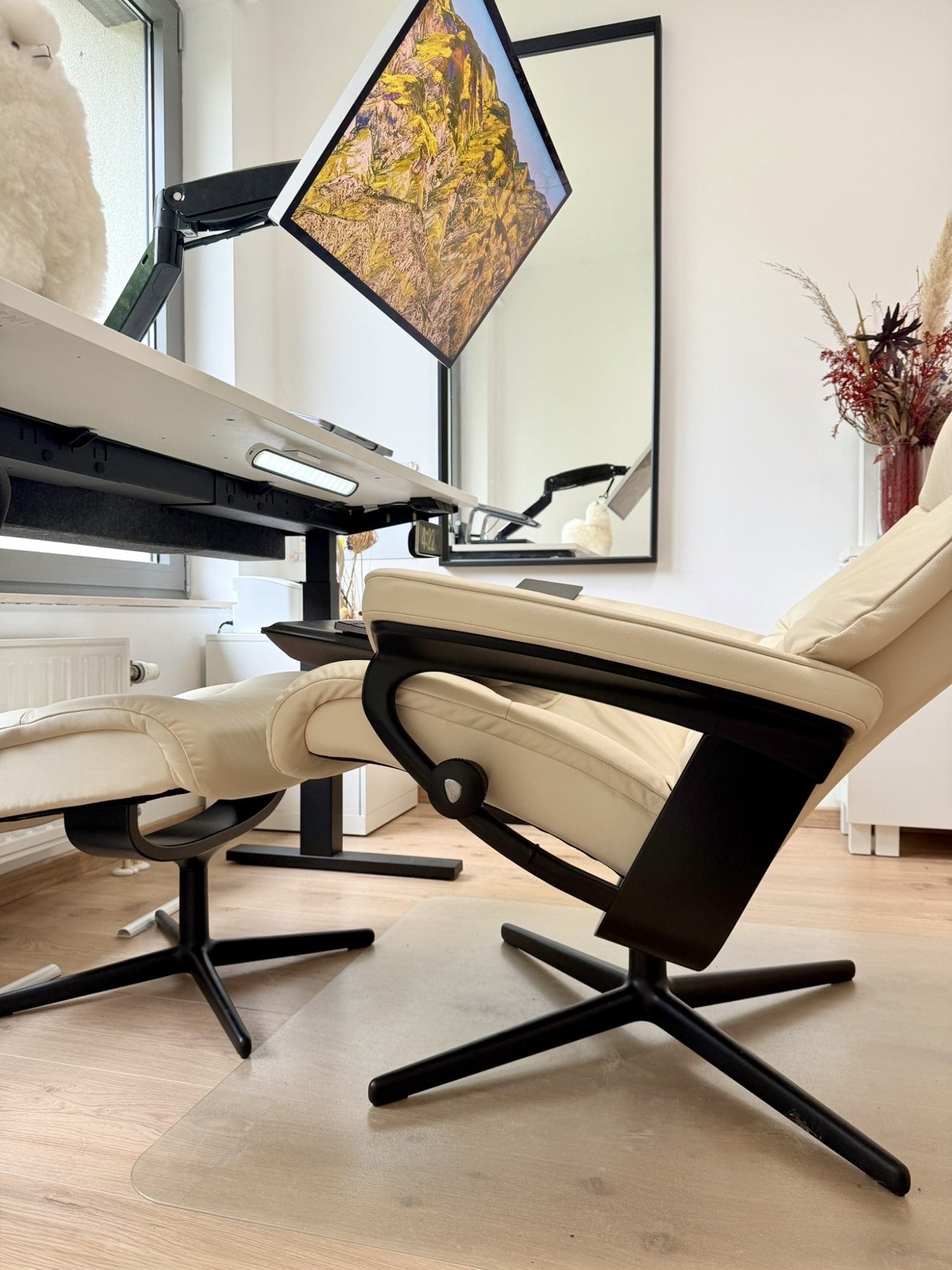 A side view of a beige Stressless View recliner paired with an IKEA MITTZON desk and Apple Studio Display on a Huanuo monitor arm