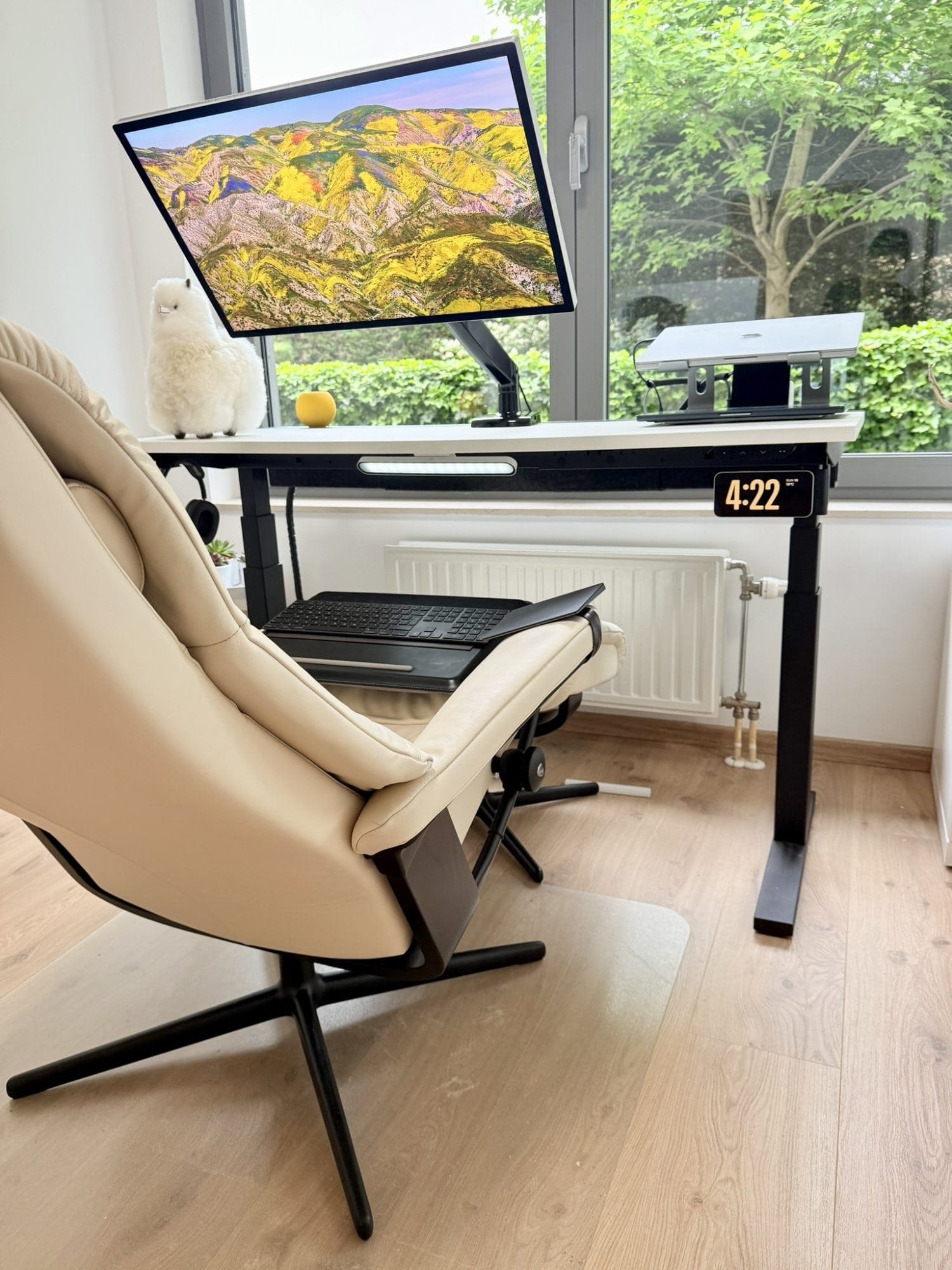 A Stressless View chair facing an IKEA MITTZON desk with an Apple Studio Display on a Huanuo arm, MacBook Pro 16″ M1 Pro on a Nulaxy stand, and a plush alpaca by the window