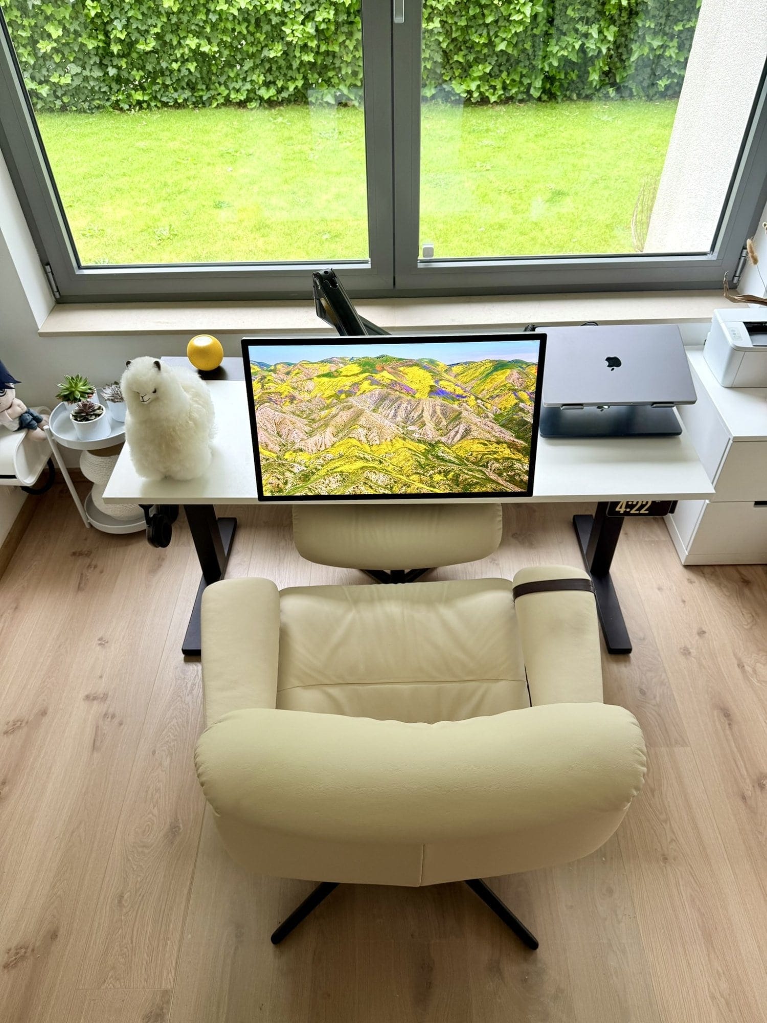 A home office setup with an Apple Studio Display, alpaca plush toy, and tilting chair
