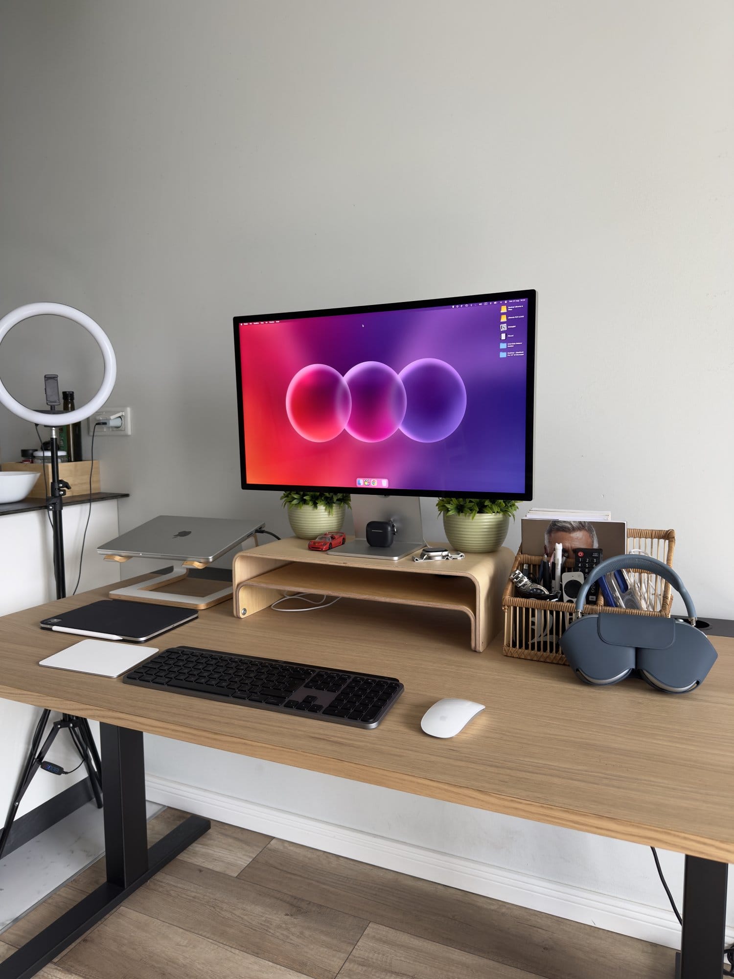 Clean desk setup with wooden monitor stand, MacBook, iPad, wireless keyboard, Magic Mouse, and headphones