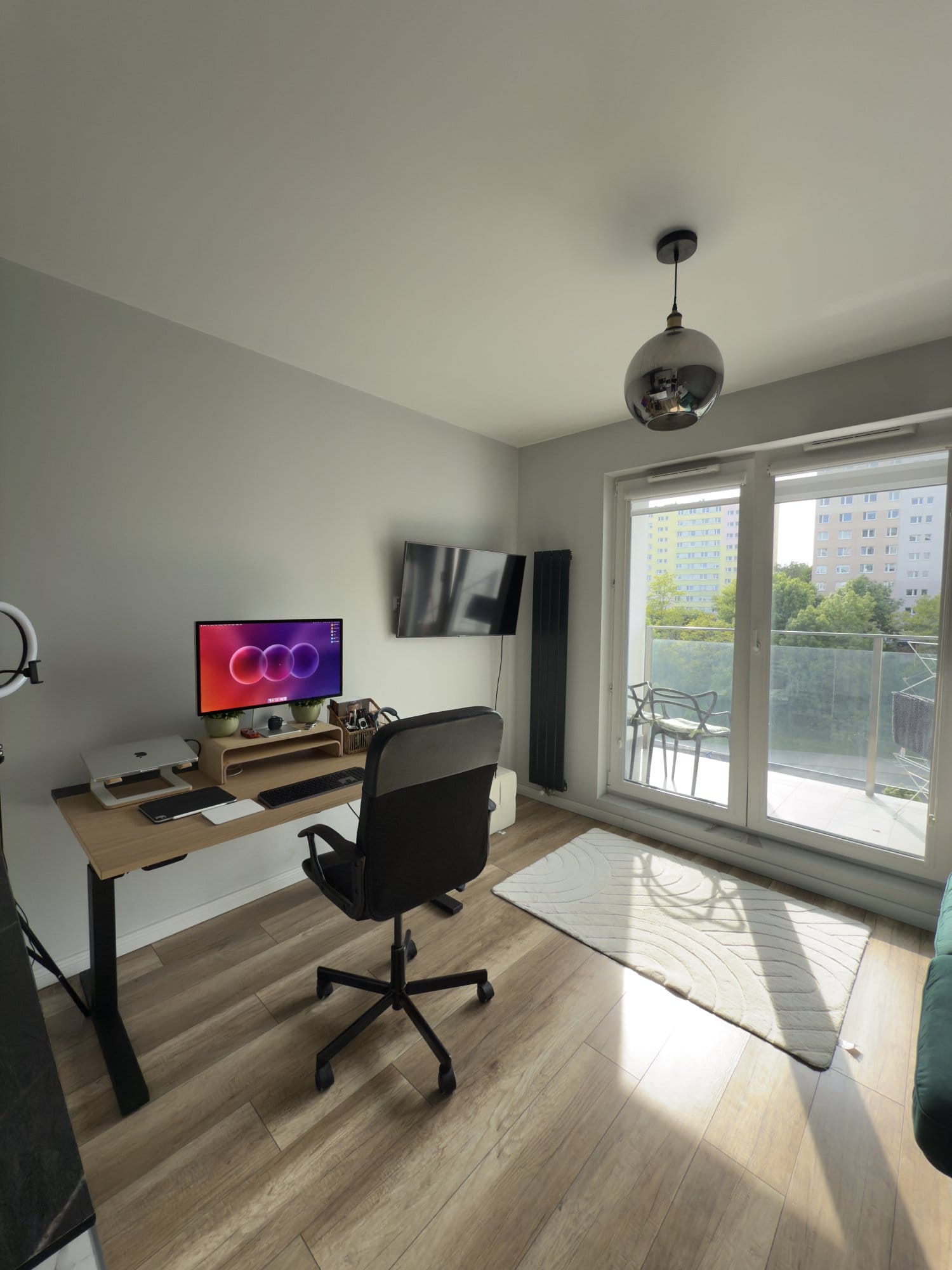 Minimalist home office with wooden desk setup, ergonomic chair, large monitor, and balcony view in natural daylight