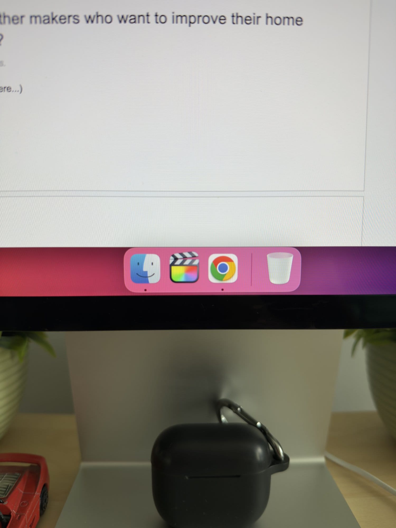 Close-up of Apple Studio Display stand with black AirPods case and macOS dock icons.