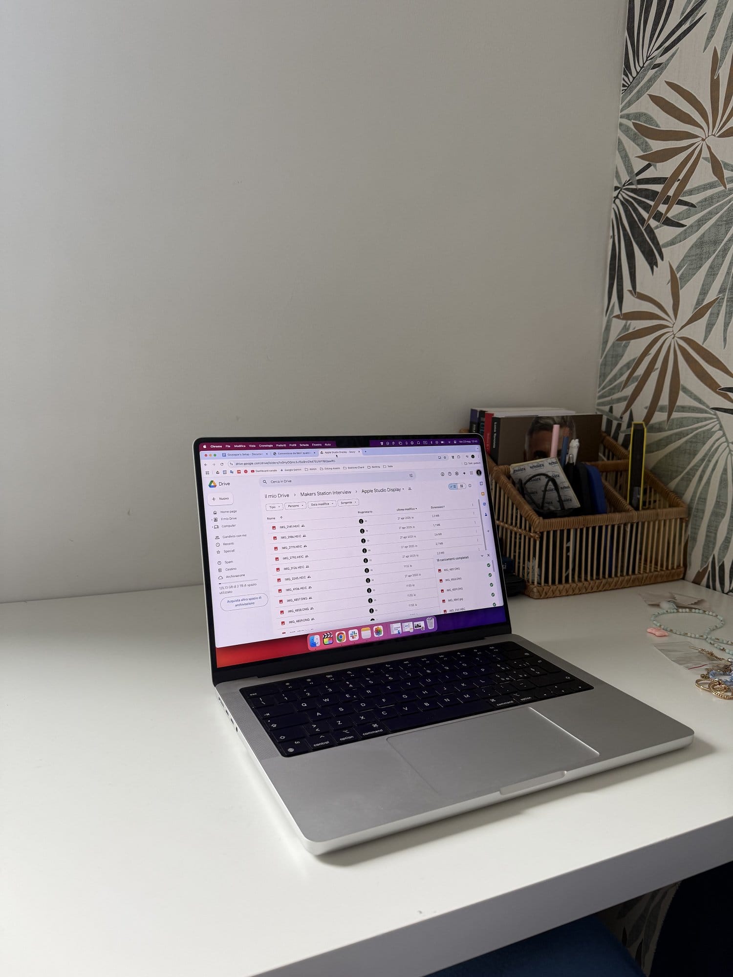 Minimal home office desk setup featuring a MacBook Pro on a clean white desk, with a rattan organiser, stationery, and patterned wallpaper