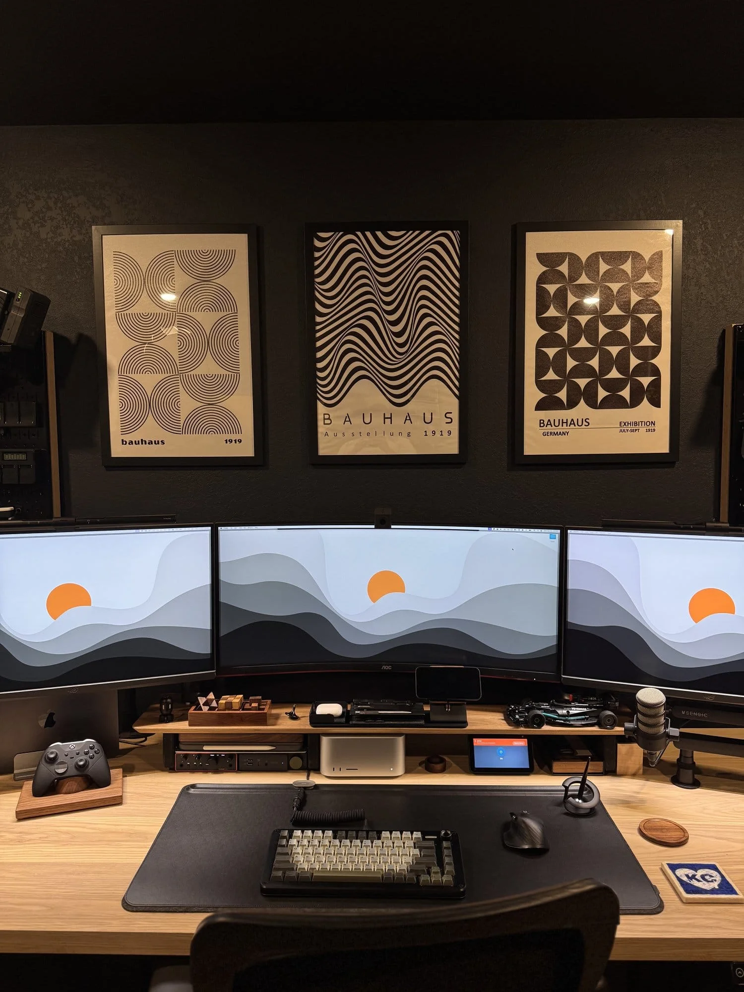 roductivity desk setup with triple curved monitors, custom mechanical keyboard, studio microphone, gaming controller, and minimalist Bauhaus wall art
