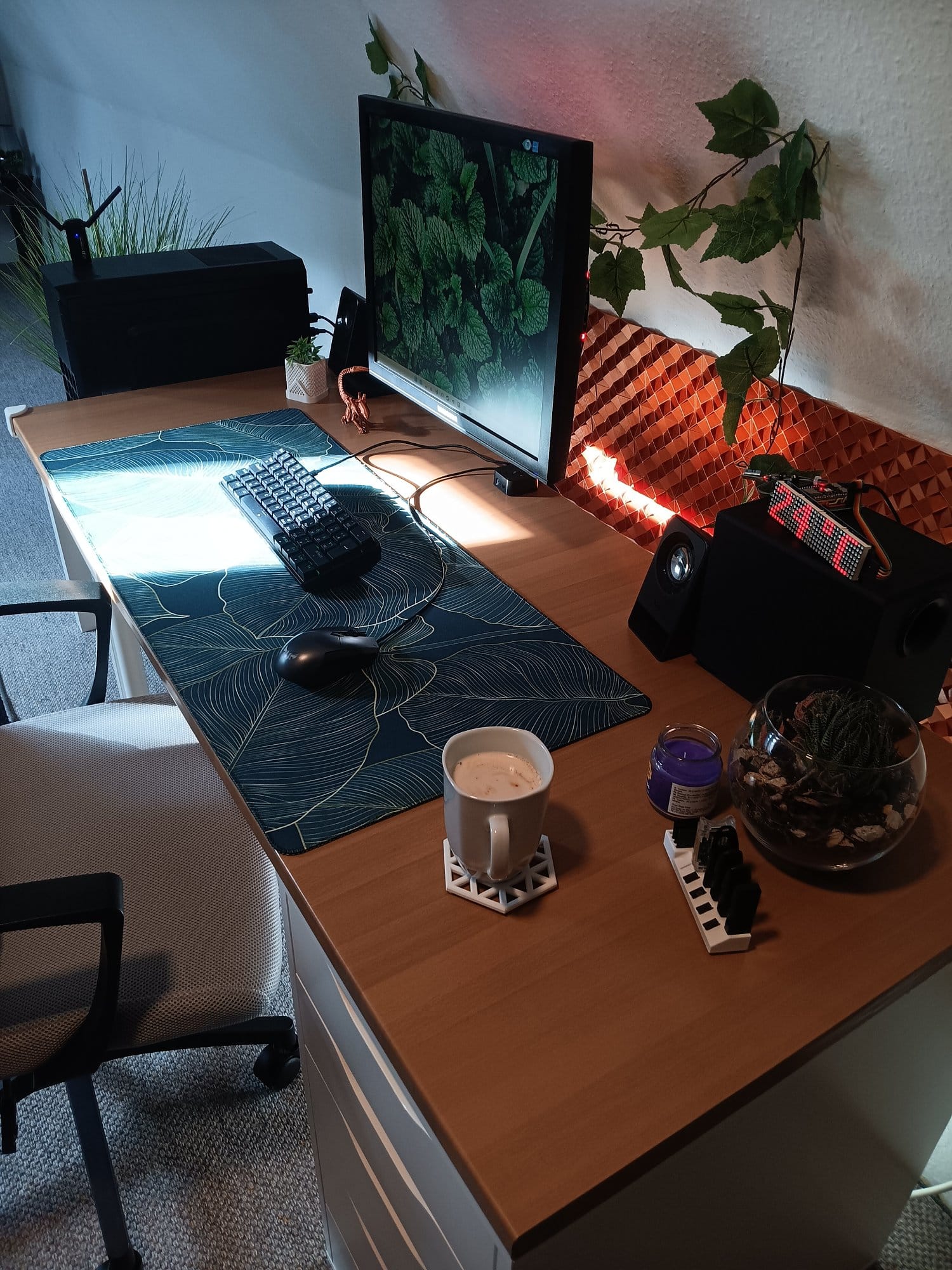 a minimalist desk setup with a leafy desk mat, mechanical keyboard, single monitor, Logitech speakers, plants, and a cup of coffee