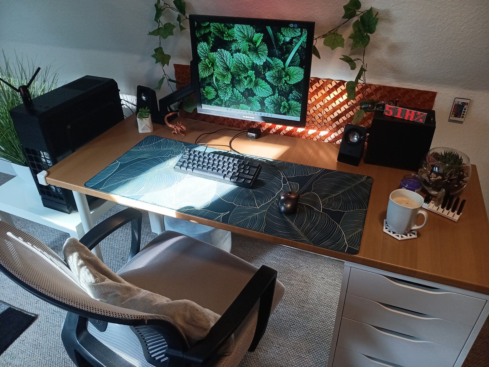 cosy workspace with single monitor, mechanical keyboard, ergonomic chair, plants, LED clock display, and a coffee mug on a wooden desk