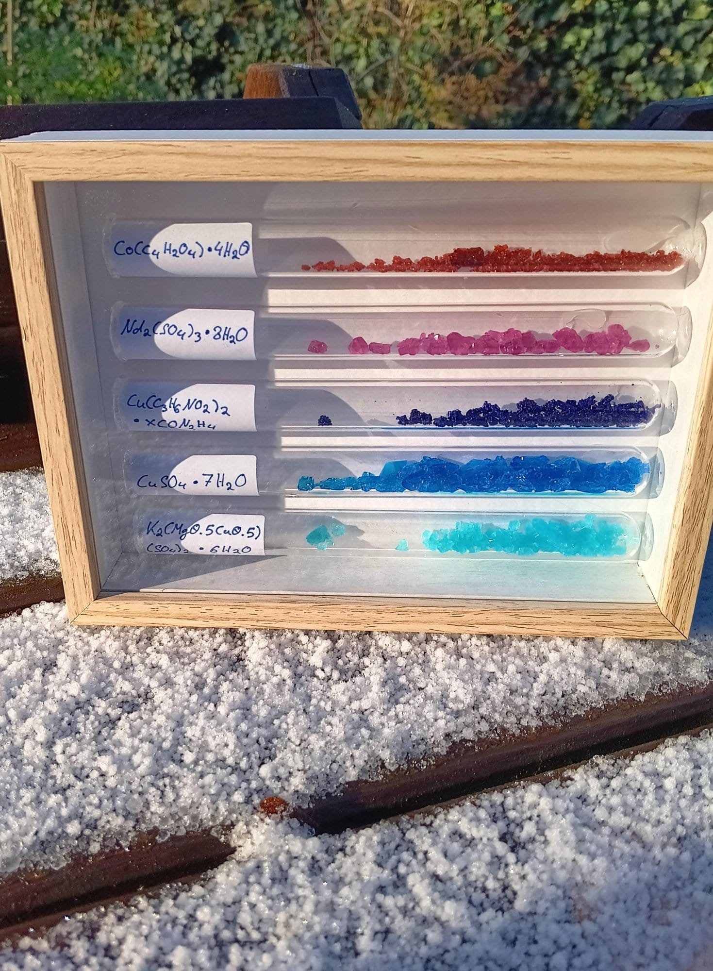 test tubes with colorful crystalline chemical samples displayed in wooden frame