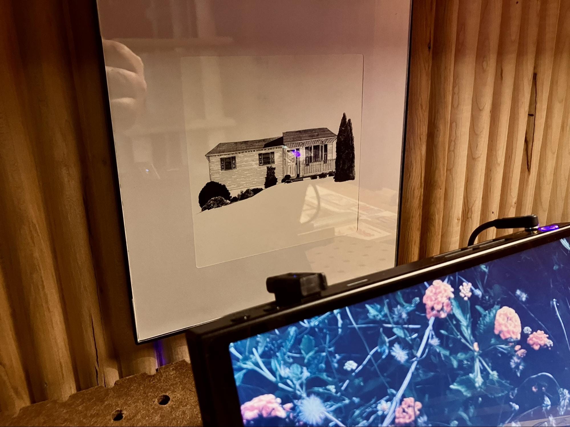 framed black and white house drawing hanging on wood panel wall behind desk setup