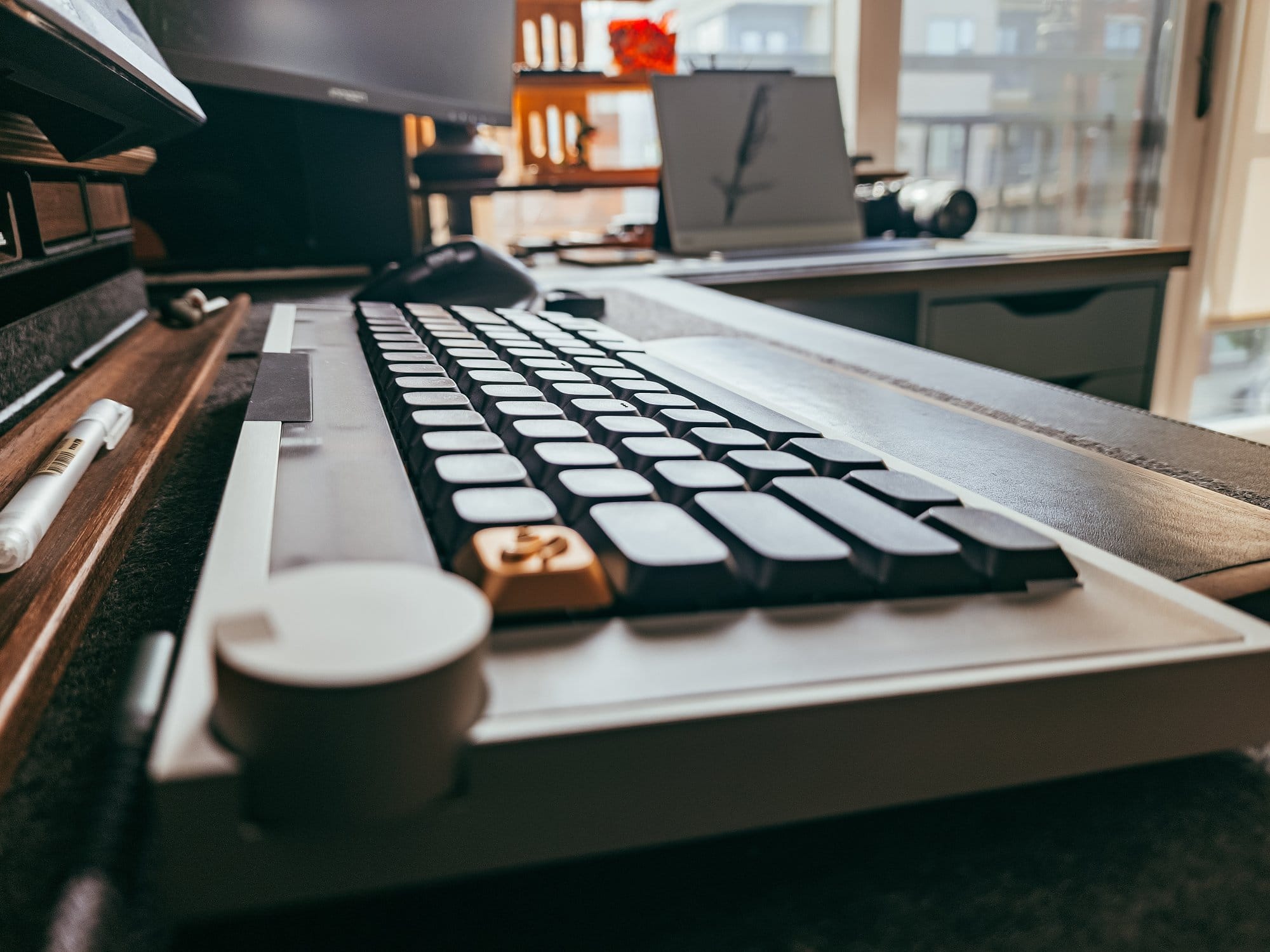 geist by geistmaschine mechanical keyboard with black keycaps, artisan brass key, control knob, and wooden wrist rest on a felt desk mat
