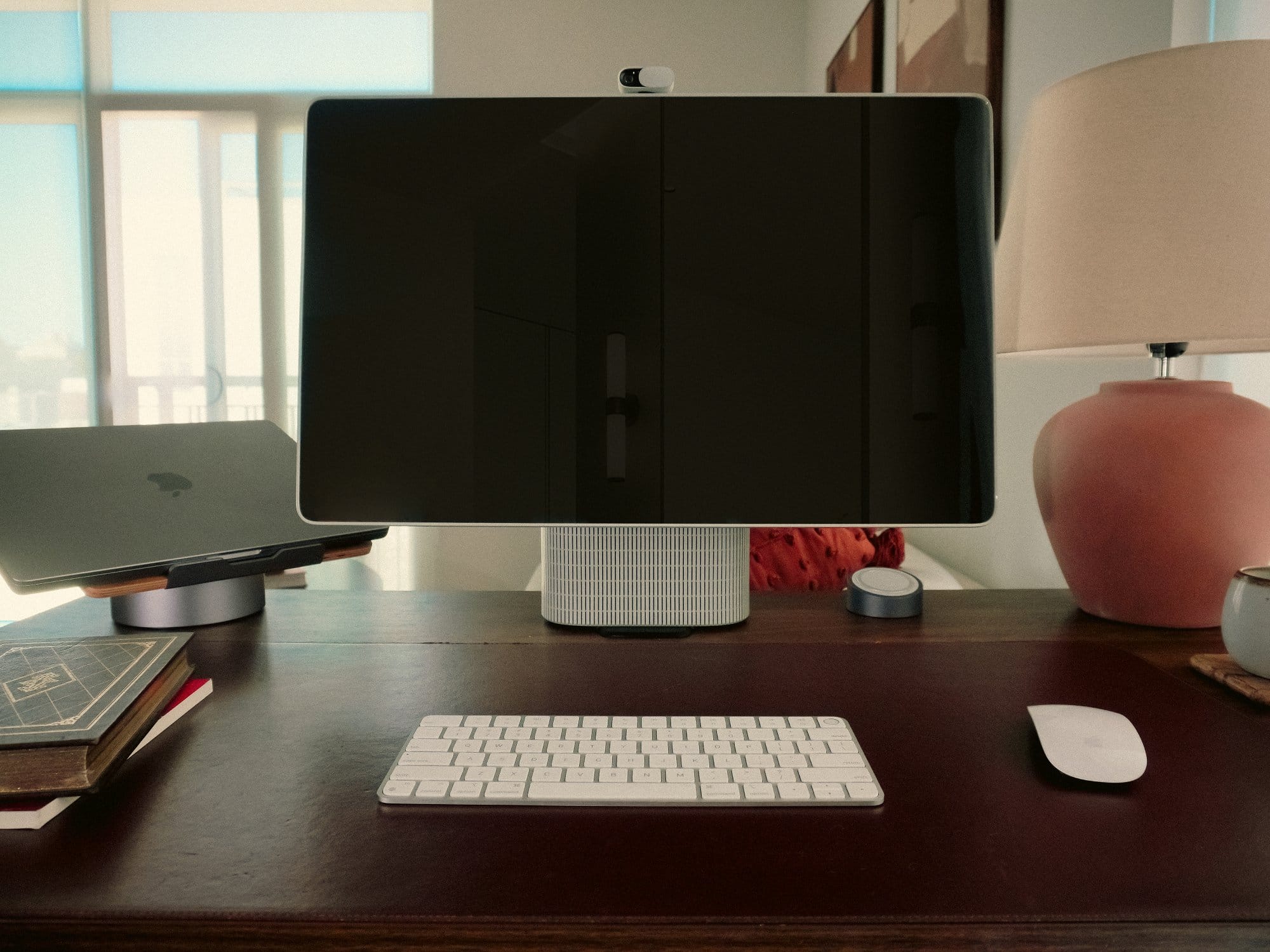 modern desk setup featuring the HomeTechCo Home Display alongside a laptop, books, and a lamp on a wooden desk