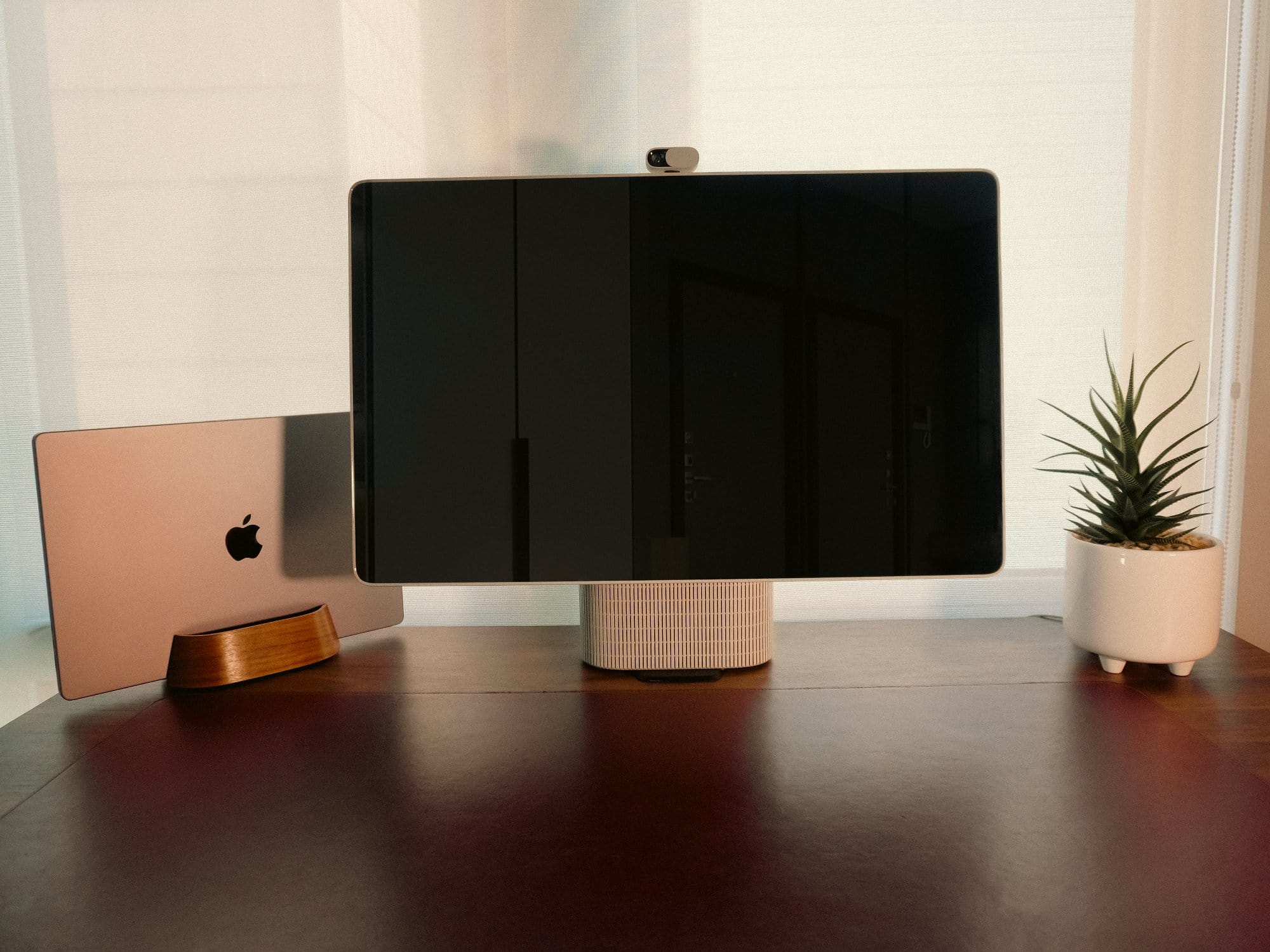 desk setup with the HomeTechCo Home Display, a closed laptop in a wooden stand, and a small potted plant